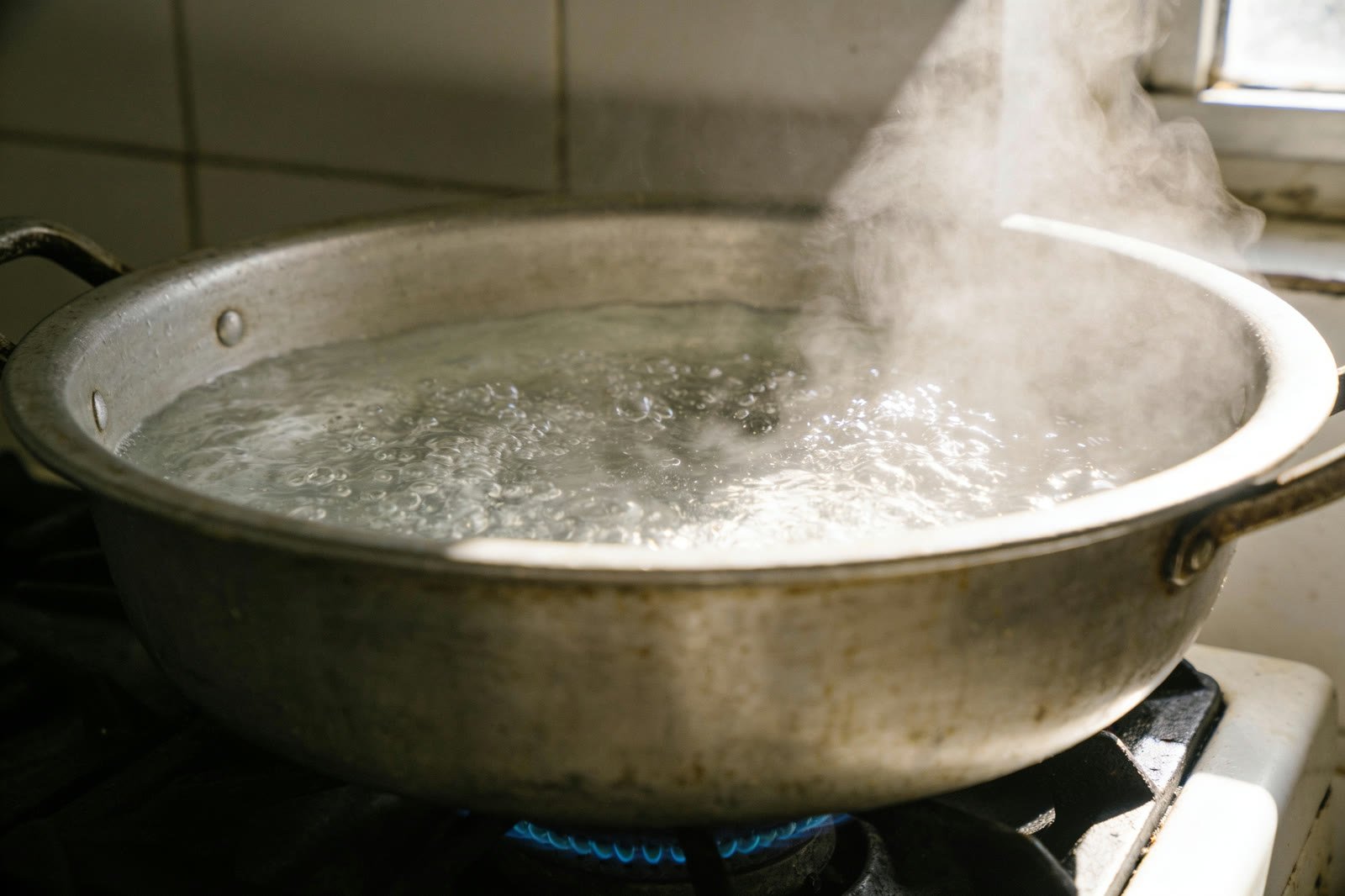 Une grande casserole d'eau salée en pleine ébullition sur le gaz, la vapeur qui monte dans la lumière.